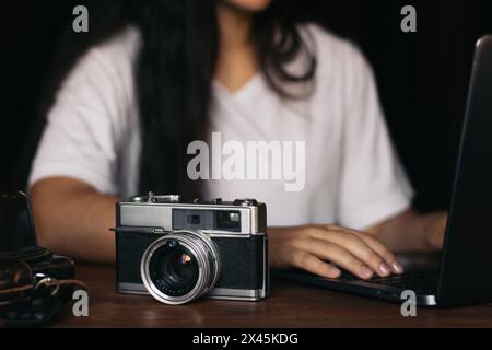 Primo piano di una telecamera analogica su un tavolo di legno. In background, una donna irriconoscibile utilizza un notebook. La vecchia tecnologia e la nuova tecnologia si uniscono Foto Stock