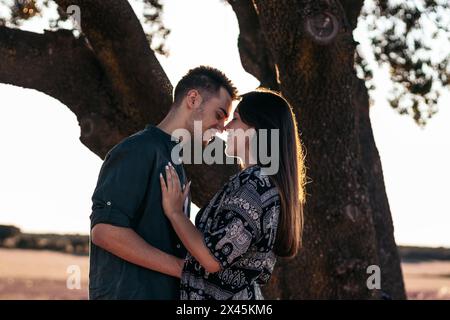 Giovane coppia che si gode una bella e soleggiata giornata in campagna. Si stanno baciando e abbracciando, felici di stare insieme Foto Stock