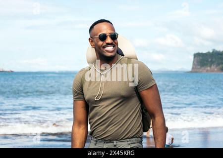 Ritratto di un uomo afroamericano che indossa occhiali da sole e cappello in un paesaggio marino in una giornata di sole Foto Stock