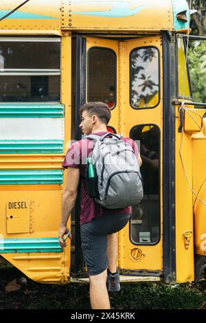 Vista posteriore di un ragazzo con uno zaino che entra in uno scuolabus Foto Stock