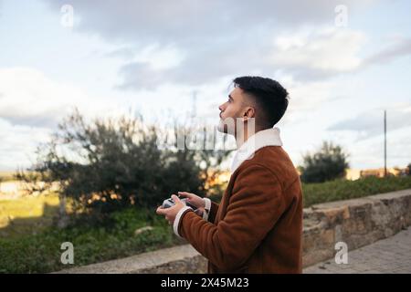 Giovane uomo che usa un drone per fotografare e registrare il paesaggio. Controlla il drone con il controller mentre guarda il cielo guardando il dr Foto Stock