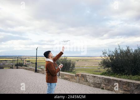 Giovane uomo che usa un drone per registrare e fotografare il paesaggio. Tiene il controller in una mano e con l'altra prenderà il drone Foto Stock
