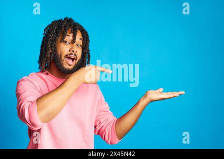 giovane con i capelli intrecciati felice di un gesto sorpreso che punta isolato su sfondo blu Foto Stock