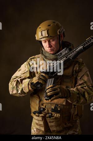 Un giovane soldato militare carica il fucile Airsoft automatico con la vista telescopica Foto Stock