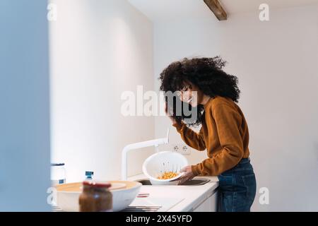 Ragazza allegra in caldo maglione e jeans che lavano ceci in colander nel lavandino mentre cucinano in cucina a casa Foto Stock