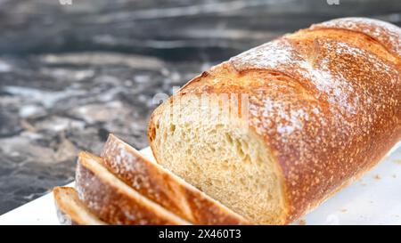 Primo piano di una pagnotta parzialmente affettata di pane di grano artigianale fatto in casa, con crosta croccante e briciola aperta. Profondità di fuoco campo limitata selettiva. Rumore g Foto Stock