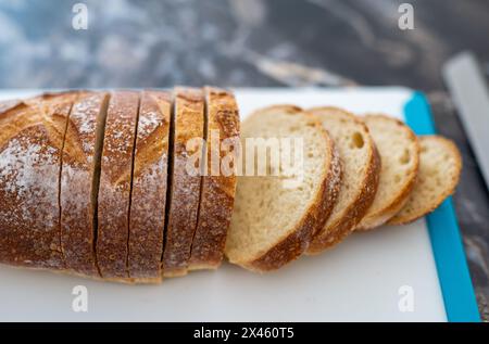 Primo piano di pane di grano artigianale fatto in casa, parzialmente affettato, con crosta croccante, briciola aperta, con tagliere. Profondità di fiel limitata selettiva Foto Stock