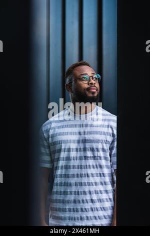 Uomo afroamericano positivo sicuro con barba e bicchieri indossare una camicia a righe casual che si affaccia sullo sfondo sfocato Foto Stock