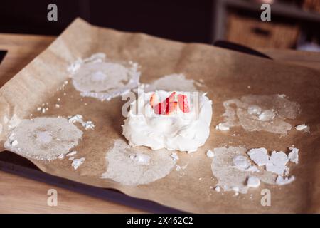 Un cucchiaio di panna montata con fragole a fette si trova su carta pergamena, circondata da farina sparsa. Questa impostazione consente di ottenere una cottura rustica Foto Stock