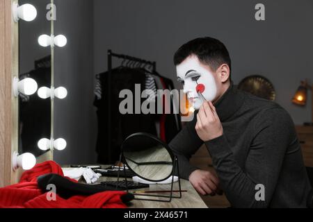 Giovane che applica il trucco mimo vicino allo specchio nello spogliatoio Foto Stock