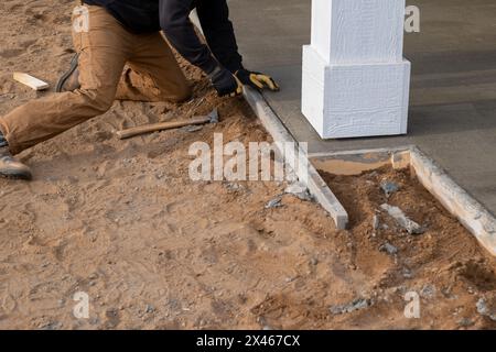 Lavoratore che rimuove la forma di legno dal bordo del nuovo marciapiede in cemento, in un cantiere edile. Foto Stock