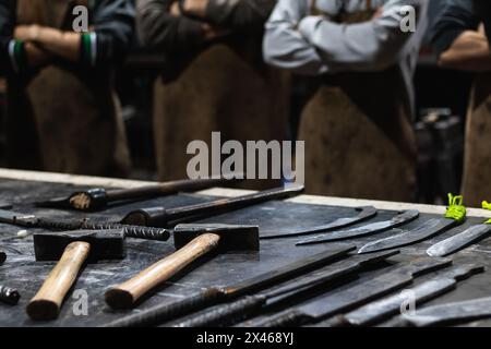 File di vari strumenti metallici posti sul tavolo in smithy con lavoratori irriconoscibili Foto Stock