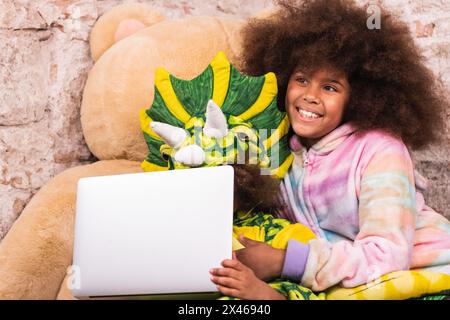Fratelli positivi in costumi unicorno e drago abbracciando e navigando computer portatile in sala giochi Foto Stock