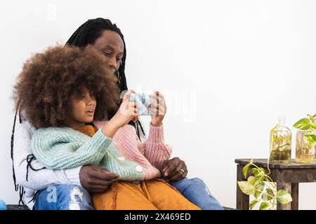 Positivo padre afroamericano hugging figlia con afro acconciatura mentre condivisione di video divertenti sul telefono cellulare Foto Stock