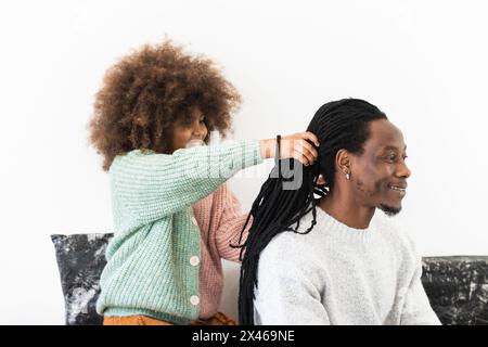 Felice figlia afroamericana facendo acconciatura al padre sorridente mentre giocare insieme Foto Stock