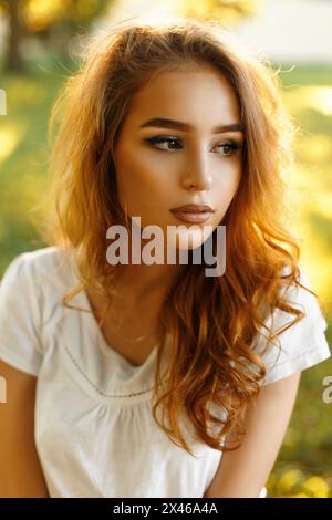 Ritratto di Una bella ragazza elegante con capelli rossi ricci in Un parco al tramonto Foto Stock