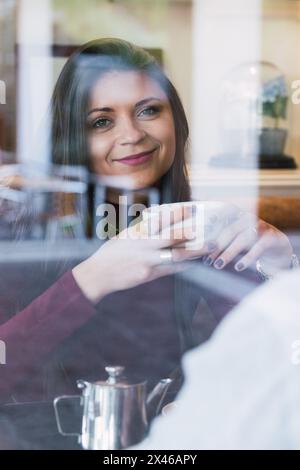 Donna felice con una tazza di bevanda calda godendo una piacevole conversazione con il ragazzo nero mentre si colazione insieme in un accogliente caffè Foto Stock