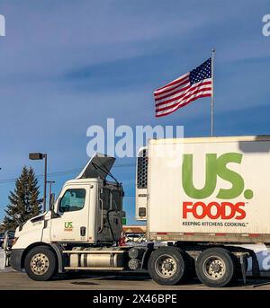 Semi-camion che trasporta merci per US Foods su strada, con una bandiera americana sullo sfondo vista sopra il rimorchio. Foto Stock