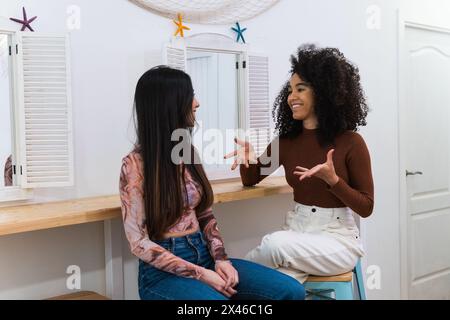 Le amiche multirazziali si sedettono al bancone al bar e si chiacchiano mentre si rilassano al bar Foto Stock