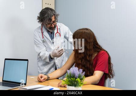 Medico di sesso maschile invecchiato che mette l'iniezione sul braccio della paziente femminile in sala medica in ospedale Foto Stock