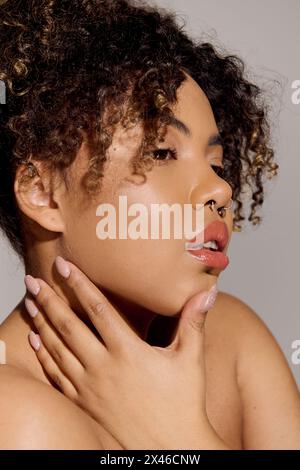 Una giovane donna afroamericana con capelli ricci, teneramente che mette le mani sul petto, mostrando cura di sé e bellezza. Foto Stock