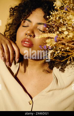 Una bella donna afroamericana con capelli ricci che tiene in mano un mazzo vibrante di fiori in un ambiente da studio. Foto Stock