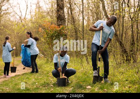 Attivisti ecologici afroamericani piantano piccoli alberi in una foresta, lavorando insieme in unità per preservare e proteggere l'ambiente naturale. Coltivazione della vegetazione per il rimboschimento. Foto Stock