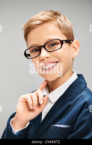 Un ragazzo con gli occhiali si mette in posa con il suo abbigliamento elegante su uno sfondo grigio. Foto Stock