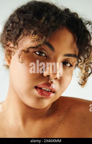 Primo piano di una donna afroamericana con un elegante anello per il naso, posa suggestiva su uno sfondo vibrante. Foto Stock