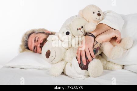 Buona notte. Bell'uomo barbuto che dorme con orsacchiotto a letto a casa. Uomo sonnolento in pigiama che dorme a letto con peluche. Bel ragazzo Foto Stock