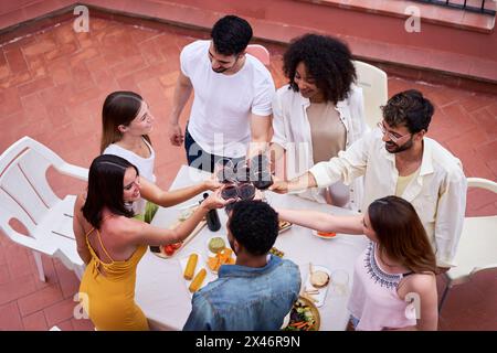 Vista dall'alto di un felice gruppo di amici che brindano con vino rosso all'aperto in una terrazza per festeggiare. Foto Stock