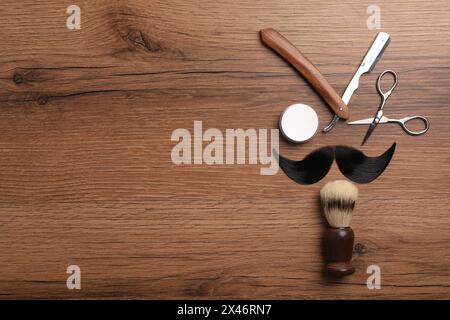 Baffi artificiali e utensili da barbiere su tavola di legno, posate in piano. Spazio per il testo Foto Stock