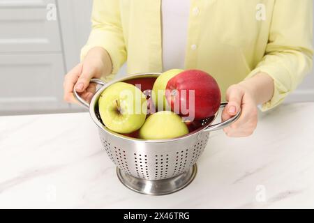 Donna che tiene il colino con mele fresche al tavolo di marmo bianco in cucina, primo piano Foto Stock