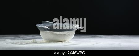 Setaccio con farina sul tavolo su sfondo nero, spazio per il testo Foto Stock