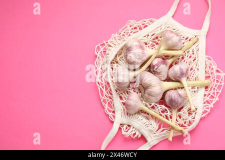 Borsa a cordoncino con teste d'aglio su sfondo rosa brillante, vista dall'alto. Spazio per il testo Foto Stock