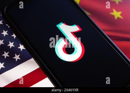 Vancouver, CANADA - aprile 30 2024 : il logo TikTok è visibile in uno schermo iPhone sulla bandiera americana e sullo sfondo della bandiera cinese Foto Stock