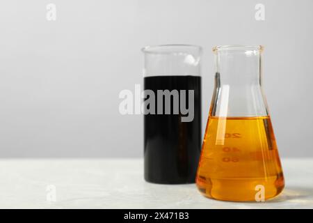 Becher e matraccio con diversi tipi di olio su tavolo bianco, spazio per testo Foto Stock