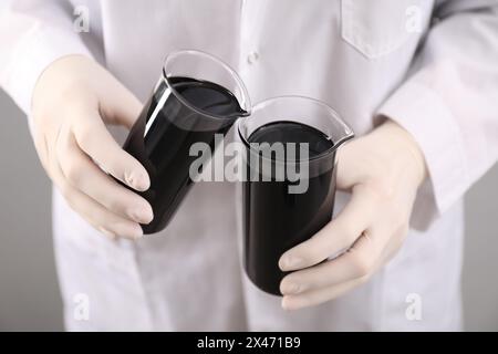 Donna che versa olio grezzo nero nel becher su sfondo chiaro, primo piano Foto Stock