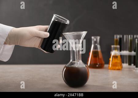 Donna che versa olio grezzo nero dal becher al matraccio sul tavolo grigio, primo piano Foto Stock