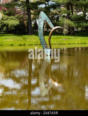 Purchase, New York – Stati Uniti – 28 aprile 2024 la moderna scultura in bronzo di Wendy Tayor, Jester, che si riflette su uno stagno nei giardini di sculture Donald M Kendall al P Foto Stock