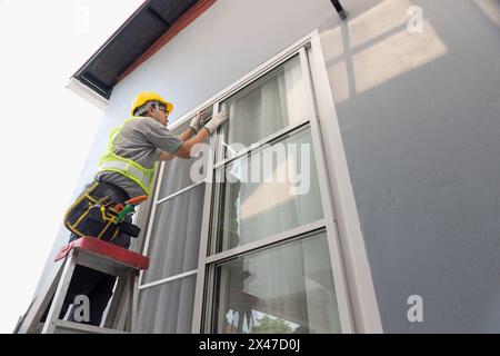 Operaio edile che ripara il finestrino scorrevole. Aprire il tappo della rotaia di regolazione. Foto Stock
