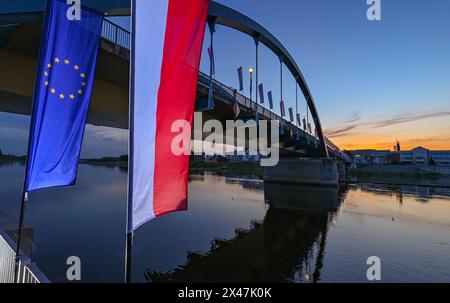 01 maggio 2024, Brandeburgo, Francoforte (Oder): La bandiera dell'Unione europea e la bandiera nazionale della Polonia ondeggiano al vento all'alba di fronte al ponte cittadino sul fiume Oder tra Francoforte (Oder) e Slubice in Polonia. In occasione del ventesimo anniversario dell'adesione della Polonia all'Unione europea, i ministri degli Esteri dei due paesi vicini intendono riunirsi a mezzogiorno. Entrambi vogliono visitare il Collegium Polonicum a Slubice sul lato polacco, nonché un festival europeo, e poi camminare insieme attraverso il ponte della città sul confine tedesco-polacco fiume Oder fino a Francoforte (Oder). Foto: Patrick Foto Stock