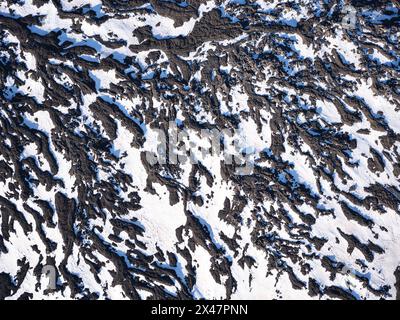 VISTA AEREA. Neve primaverile e lava scorrono sul versante settentrionale dell'Etna. Città metropolitana di Catania, Sicilia, Italia. Foto Stock