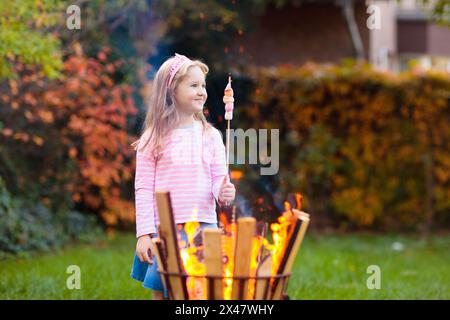 Bambino con smores al fuoco del campo. I bambini arrostiscono il marshmallow sul bastone al falò. Famiglia autunnale Foto Stock