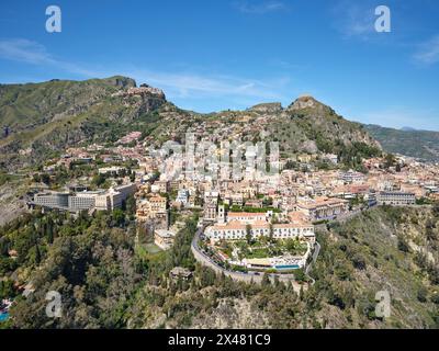 VISTA AEREA. La città turistica di Taormina, e in alto a sinistra, il paese collinare di Castelmola. Città metropolitana di Mesina, Sicilia, Italia. Foto Stock