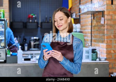 Giovane lavoratrice di servizio in grembiule con smartphone nel ristorante e nella caffetteria Foto Stock