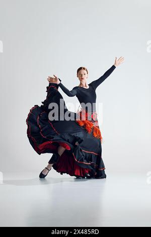 Ritratto dinamico di una ballerina, donna elegante che si esibisce con passione, ballando flamenco su sfondo grigio studio Foto Stock