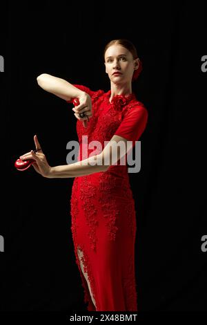 Bella donna, ballerina di flamenco con elegante abito rosso, colpisce la posa accattivante con le castanette sollevate, mettendo in risalto la danza ritmica dell'essenza. Foto Stock