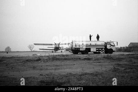 Nel 2013, un aeroporto agricolo nella città di Dongying, nella provincia di Shandong, in Cina, due persone si trovano in piedi su un camion di carburante, gestendo verso il cielo vicino a un aereo fisso guidato da elica in un campo aperto, apparentemente rurale. La foto cattura un momento di interazione tra le persone e il vasto e vuoto ambiente che le circonda, sotto un cielo coperto. Foto Stock