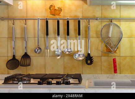Fornello di una cucina moderna con utensili appesi a un bar di metallo Foto Stock
